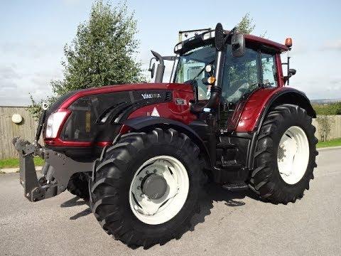 A red Valtra T153 Versu Tractor with a black cabin, visible from a side angle with its wheels on the ground.